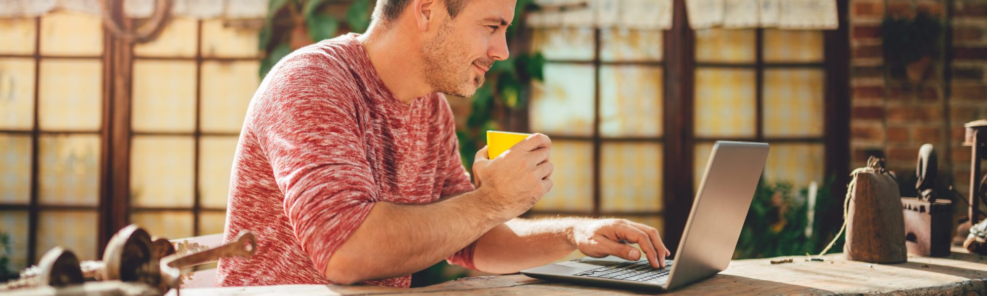 Men sitting in the at backyard patio drinking coffee and using laptop